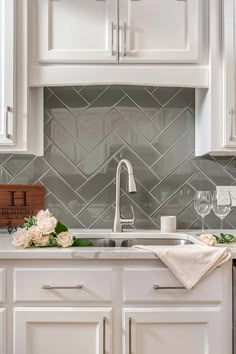 a kitchen with white cabinets and marble backsplash, wine glasses on the counter