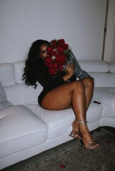 a woman sitting on top of a white couch next to a red rose bouquet in her lap