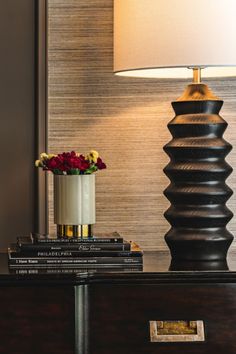 a vase with flowers on top of a table next to a lamp and some books