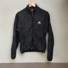 a black jacket hanging up against a wall with a blue triangle on the front pocket