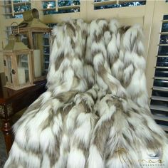 a bed covered in white and brown fur next to a table with a lantern on it