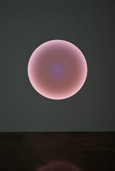 a round object sitting on top of a wooden table next to a light that is pink