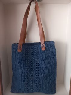 a blue knitted bag hanging from a hook on a white wall with brown leather handles