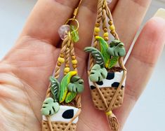 a pair of earrings with plants on them are being held in someone's hand