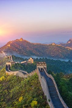 the great wall of china at sunset with mountains in the background and foggy sky