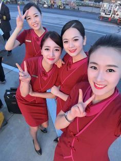 three women in red uniforms giving the peace sign while standing on an airport tarmac