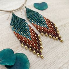 a pair of earrings with beads and leaves on a table next to a blue leaf