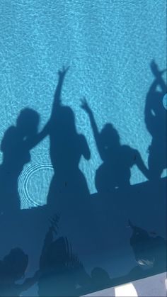 the shadow of two people standing in front of a swimming pool with their hands up