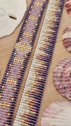 two purple and yellow beaded bracelets next to seashells on a table