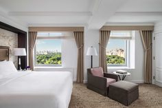 a hotel room with a large bed and two chairs in front of a window that overlooks the city