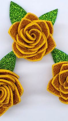 three yellow flowers with green leaves and glitters on them, sitting next to each other