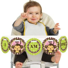 a baby sitting in a high chair with his hand up to the camera and smiling