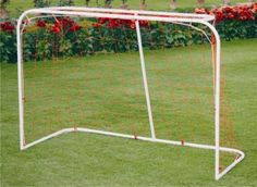 a white soccer goal in the grass with red flowers behind it on a sunny day