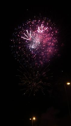 fireworks are lit up in the night sky above a street light and cars on the road