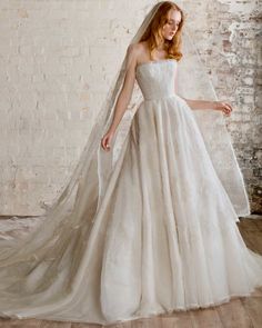 a woman wearing a wedding dress and veil in front of a brick wall with white paint