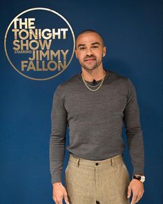 a man standing in front of a blue wall with the tonight show logo on it