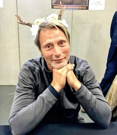 a man sitting at a table with his hand on his chin and wearing a deer antlers'headband