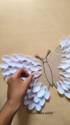 someone is making a paper butterfly out of white flowers on a piece of brown cardboard