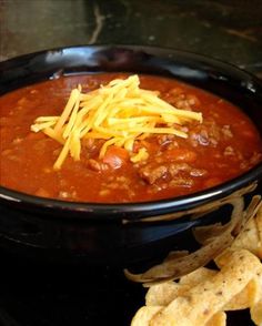 a black bowl filled with chili and cheese next to tortilla chips on a table