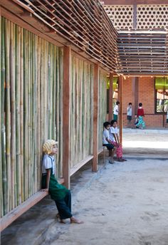 a group of people standing next to each other in front of a bamboo building with wooden slats on the roof