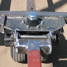 a metal object sitting on top of a dirt ground next to a red handle and tire