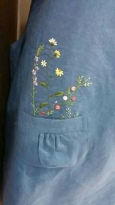 a blue shirt with flowers painted on the front and back pocket, sitting on top of a bed