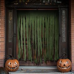 two carved pumpkins sitting in front of a door with green curtains on it's side