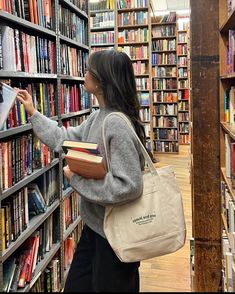 a woman is looking at books in a book store while holding a tote bag