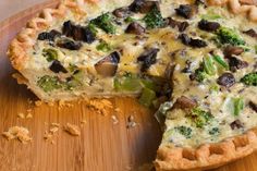 a quiche with broccoli, mushrooms and other vegetables on a wooden cutting board