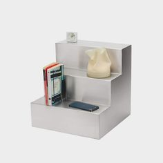 a white shelf with two books and a cell phone on it, next to a vase