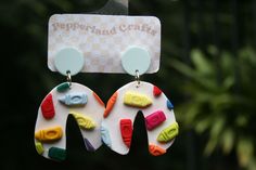 a pair of colorful earrings hanging from the side of a card board that says pepperland crafts