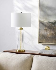 a table lamp sitting on top of a wooden table next to a white couch and painting