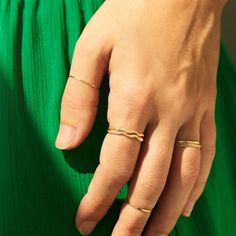 A hand rests in front of vibrant green fabric. The hand is wearing dainty gold rings stacked on eachother for a bolder look. Gold Tiny Midi Rings Fine Jewelry, Modern Twist 14k Gold Stackable Rings, Minimalist Yellow Gold Snake Ring, Minimalist Yellow Gold Open Snake Ring, Gold Minimalist Snake Ring For Promise, Elegant 14k Gold Snake-shaped Ring, Gold Minimalist Snake Ring As Promise Ring, Elegant 14k Gold Snake Shaped Rings, Gold Midi Rings With A Modern Twist