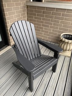 a black plastic chair sitting on top of a wooden deck next to a brick wall