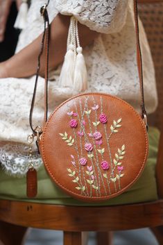 a woman is sitting on a chair holding a purse with flowers painted on the side