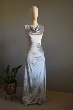 a mannequin wearing a silver dress next to a potted plant on a wooden floor