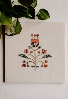 a white canvas with embroidered flowers and leaves on it next to a potted plant