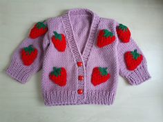 a pink knitted sweater with strawberries on the front and back, sitting on a white surface