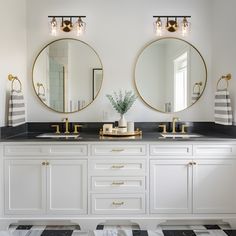 two round mirrors are above the double sinks in this white and black bathroom with gold accents