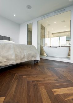 a bedroom with wood flooring and white bed in the corner next to a bathtub