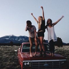 three girls standing on the back of a red truck with their arms in the air