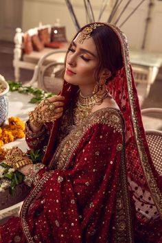 a woman in a red bridal outfit sitting at a table with flowers on it