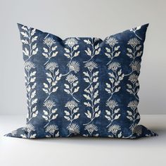 a blue and white pillow with leaves on the front, sitting on top of a table