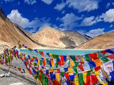 there are many colorful flags hanging on the side of this mountain lake and mountains in the background