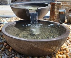 an outdoor fountain with water running from it's sides into the ground, surrounded by rocks and gravel