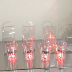 several shot glasses sitting on top of a glass table with red lights in the middle