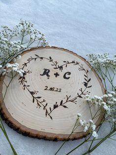 a wooden slice with the initials and date engraved on it is surrounded by flowers in front of snow