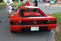 a red sports car is parked on the side of the road with people walking by