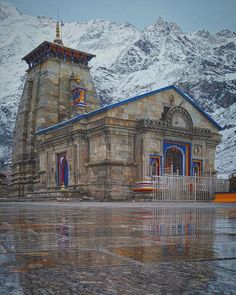 an old building in the middle of mountains with snow on it's top and blue trim