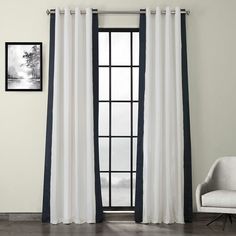 a white and black curtain hanging on a wall next to a chair in front of a window